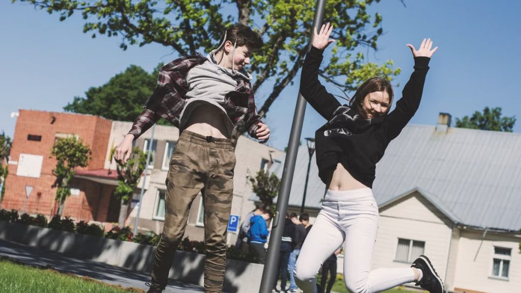 Two teenagers joyfully jumping outdoors in Šiluva, Lithuania under a bright blue sky. Captured in springtime.