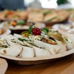 A wooden platter of assorted vegetarian wraps with fresh ingredients, perfect for parties.