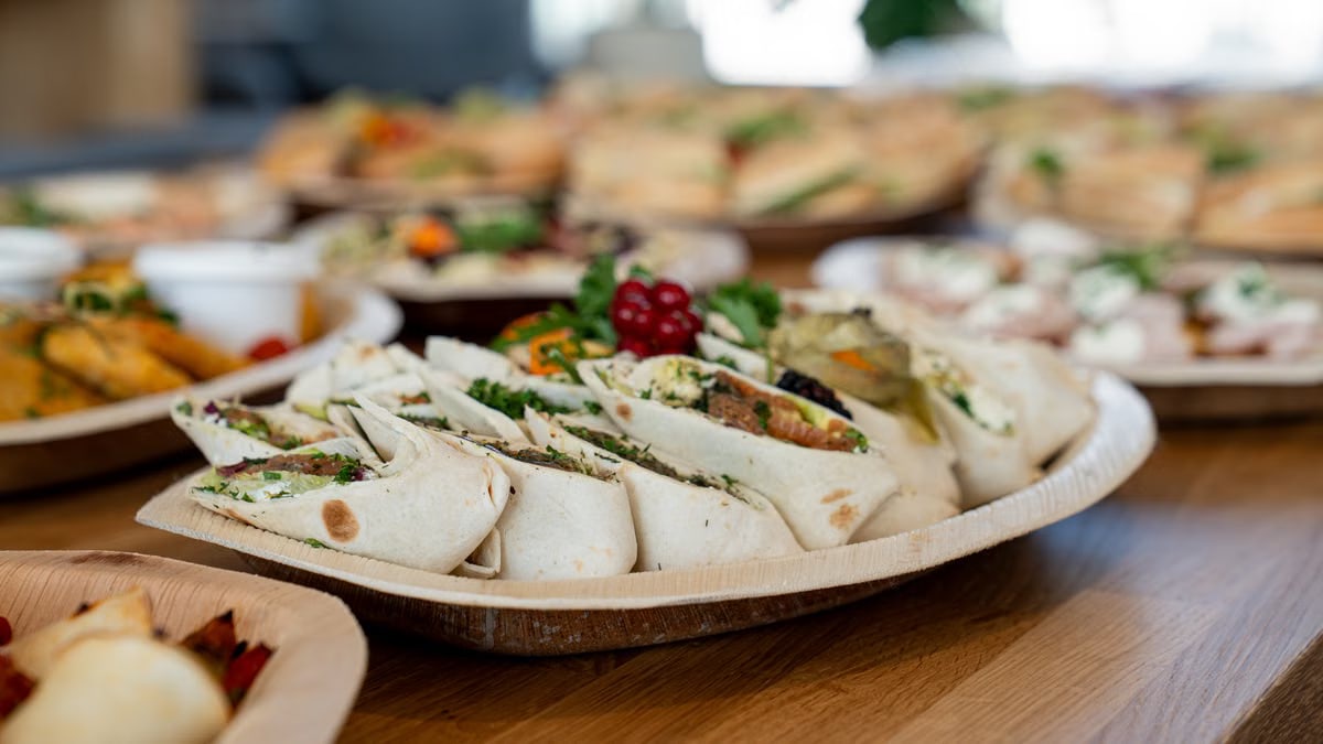 A wooden platter of assorted vegetarian wraps with fresh ingredients, perfect for parties.